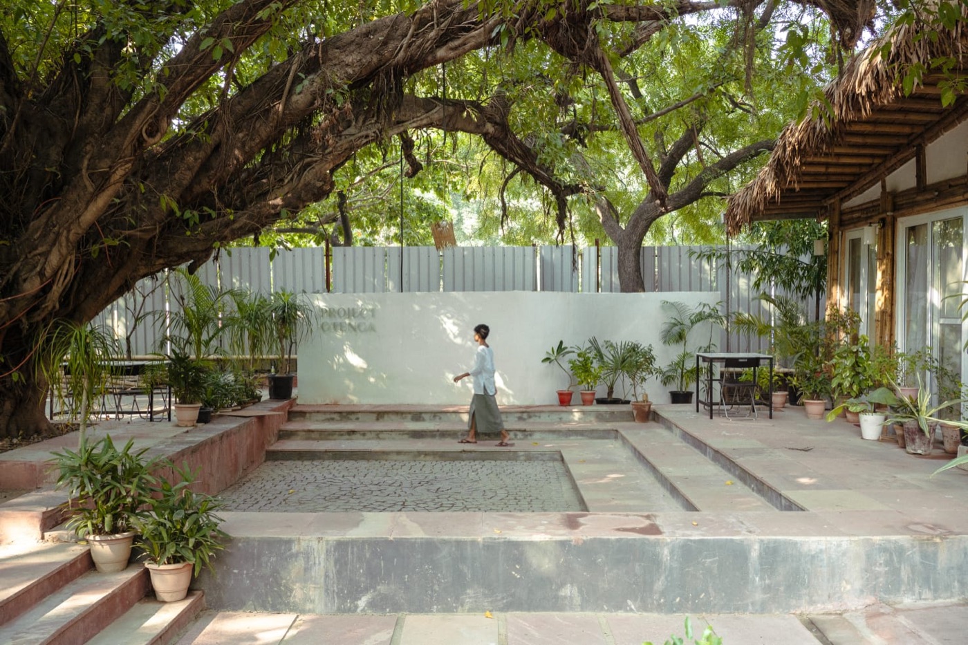 Project Otenga: the courtyard under the Pilkhan tree, the bamboo-and-thatch structure, and the signed wall (1 of 4)
